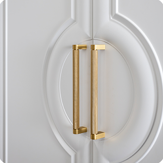 Close-up of an elegant cabinet door featuring a white, intricately molded design with a pair of sleek, gold rectangular handles. The hardware adds a touch of luxury and sophistication to the classic decorative paneling, making it a standout element in any interior design.