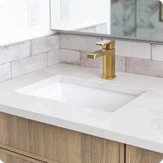 Contemporary bathroom sink area with a rectangular under-mount sink and a brushed gold faucet, set against a textured subway tile backsplash and light wood cabinetry, highlighting the luxurious and functional design elements.